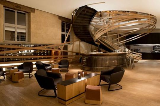 lumen-4-les-haras | LightNOW AWARD OF MERIT Les Haras Strasbourg   Lighting Designer: L’Observatoire International Herve Descottes, Solenn Borchers, and Etienne Gillabert Interior Designer:	 Agence Jouin Manku Having spent its first 150 years as the historic National Stud Farm of Strasbourg, this beautiful structure has been reborn as Hotel Les Haras Strasbourg, a luxury hotel located in the city center. Inside, the bronze tones of custom-design fixtures play off of and compliment the exposed-wood, rich brown color palette and earthy textures of the interior, all of which harken back to its previous life as a stable. In the hotel’s Brasserie restaurant, integrated linear LEDs and custom-designed hanging cylindrical fixtures provide an intimate ambiance that perfectly tempers the vast, airiness of the space. Exuding warmth and sensuality, the light design melds old and new in this arresting space.